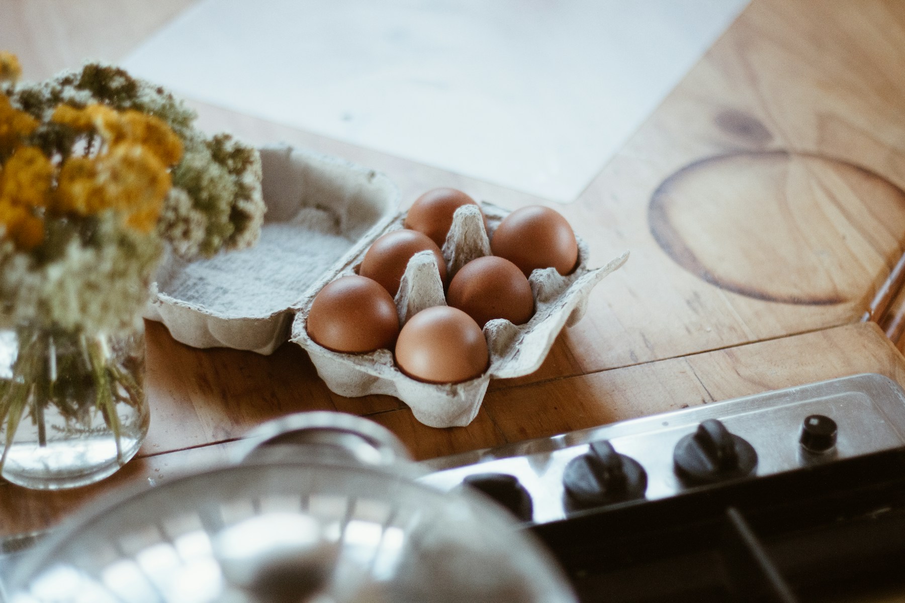 Brown eggs in a paper carton on a warm wooden kitchen counter